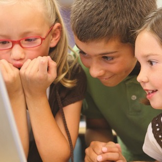 Three children view a computer screen together.