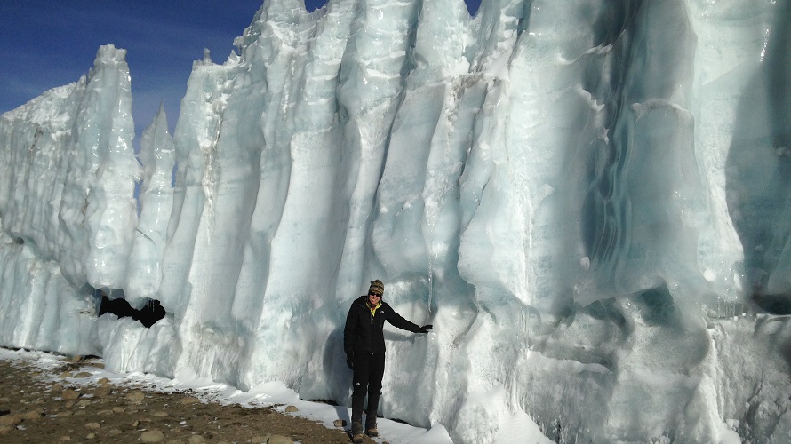 A woman stands next to a glacier.