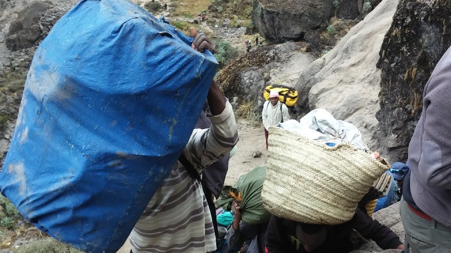 Porters carry bulky and heavy items while climbing a mountain