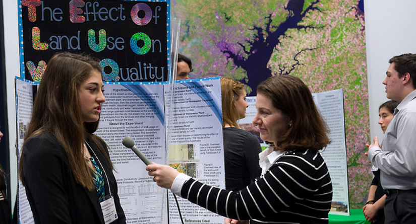 A woman interviews a girl student about her science fair project.