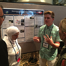 A student explains his science fair project to onlookers.