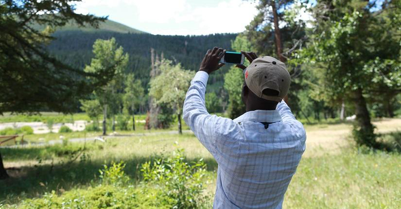 A man taking a picture of the sprawling green landscape ahead.