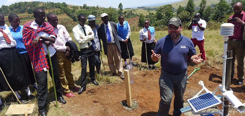 GLOBE trainer explaining a protocol outside to a group of teachers, standing next to scientific instruments.