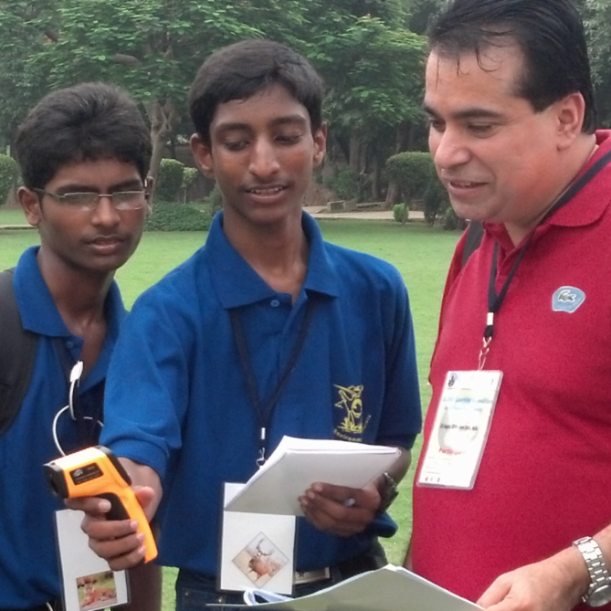 A GLOBE educator and two students stand outside. The educator holds a notepad and a scientific instrument.