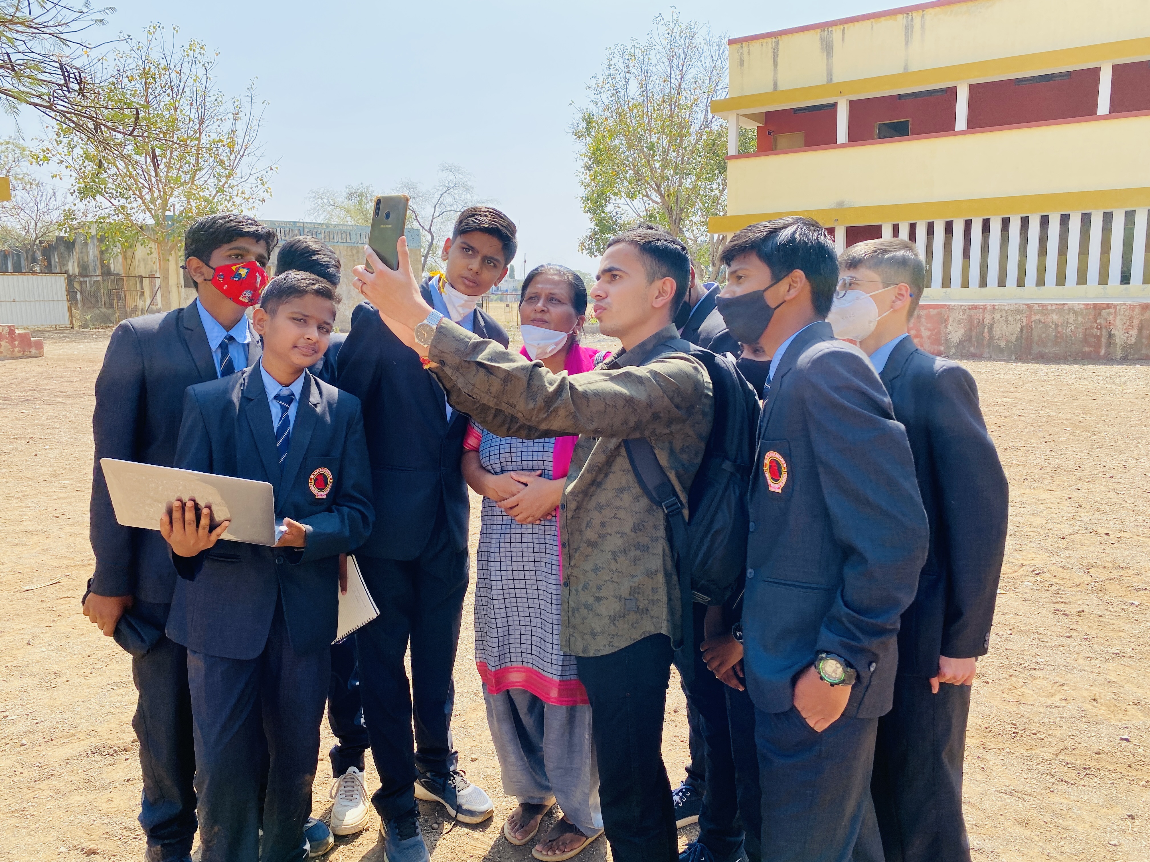 Yashraj Patil shows something on his phone to several students outside.