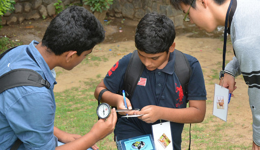 Three students collect environmental data outside, using instruments.