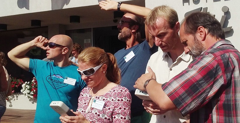 A group of teachers look up at the sky, while another takes atmosphere measurements with an instrument.