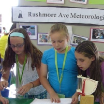 Three girl students bend over a table to read out-load their presentation on meteorites.