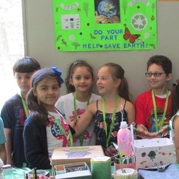 Three girl and two boy students pose below a green poster advising the reader to save the Earth.