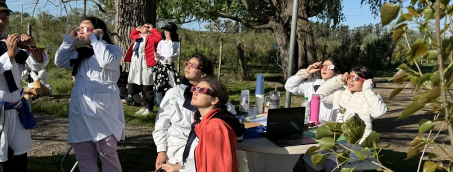 Two students wearing life jackets stand by a lake, holding a tube for measuring water data.