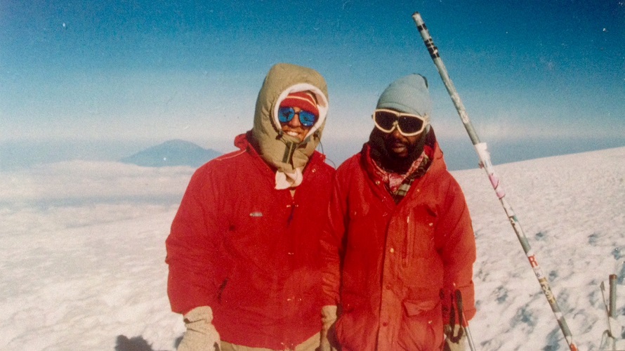 Two men pose for a photo on Mt. Kilimanjaro with another mountain in the background.