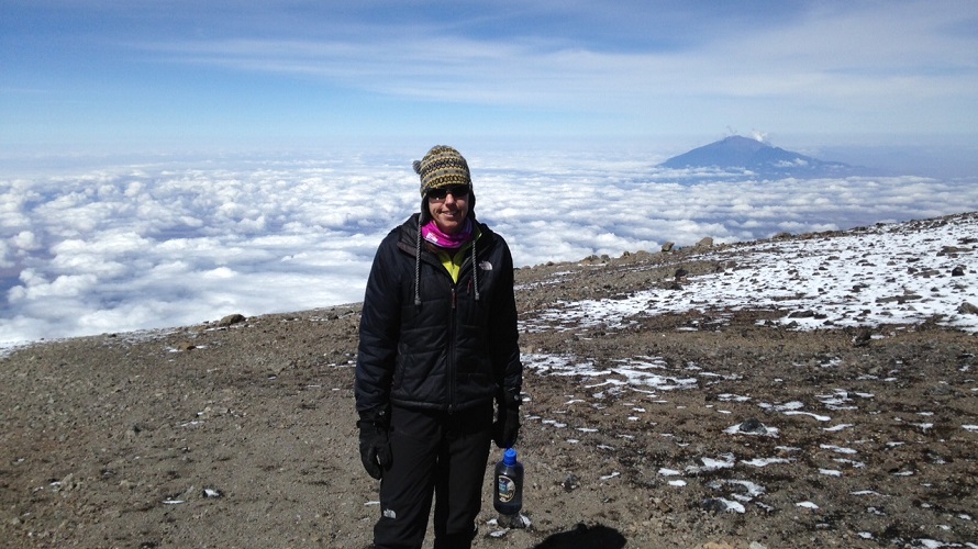 A woman stands on top of a mountain with another mountain in the background.