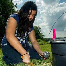 A girl crouches to take soil samples.