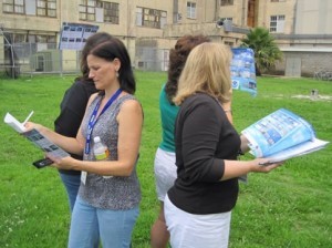 Women standing in a circle back-to-back looking at papers. 