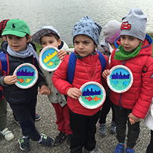 Young students hold up a paper plate craft that they made at an event.