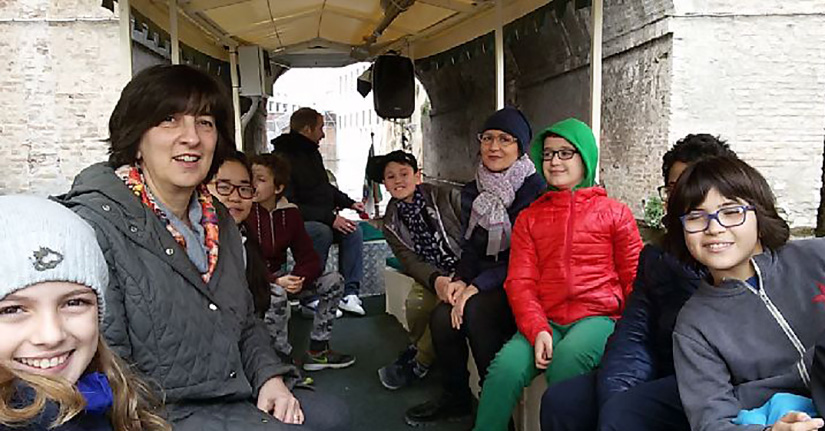 Children and a teacher smile for a photo while sitting on a boat.