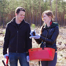 Two teachers look at a young tree planting.