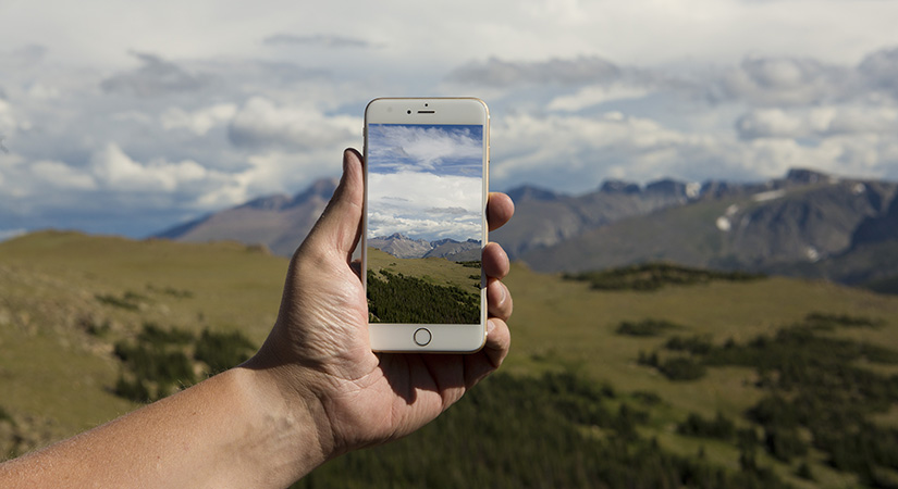 A hand holds a smart phone to take a picture of the landscape.