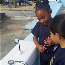 Two students stand and measure solar noon with a compass.