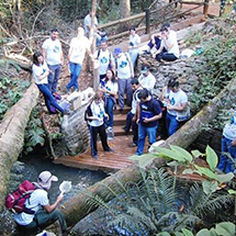 Students and teachers sit and stand near a river.