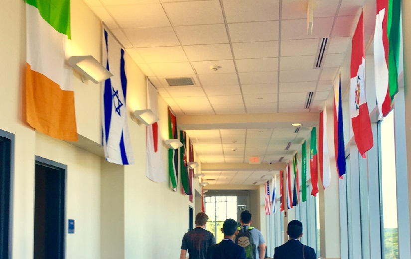 A view of international flags lining a hallway.  Four young men walk down the hallway with their backs turned to us.