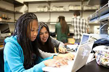 Students look together at a laptop.