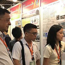 A man looks on as two students explain their science poster.