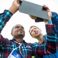 Two men are looking at a tablet that is being held up, with the sky being the background.
