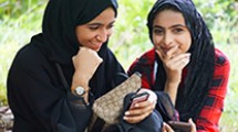 Two girls smile and hold smart phones.