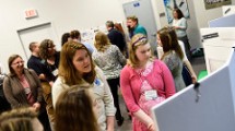 A woman ans several girls look together at their science fair project.