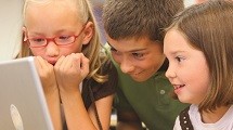 Three children look at a computer screen together.