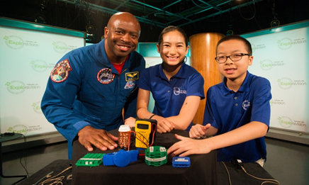 A man standing with two students, all wearing NASA shirts, standing behind a table with a project.
