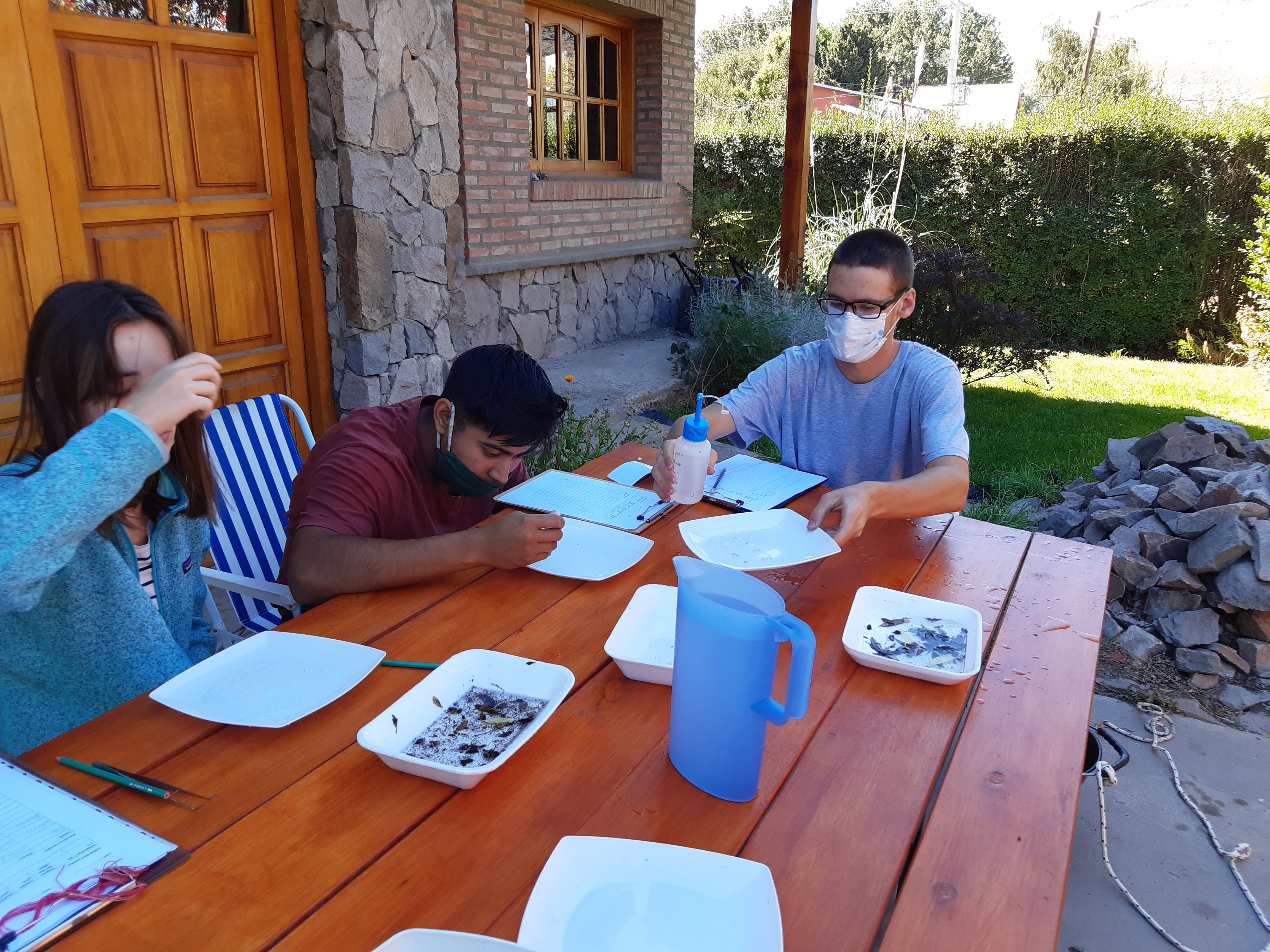 Photo of GLOBE Argentina students Marianela P., Juan W., and Lucio M., working around an outdoor table