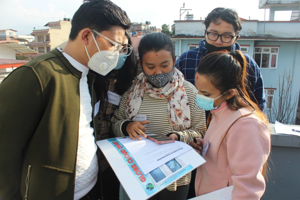 Five people in masks, stare at papers held by the woman in the center.