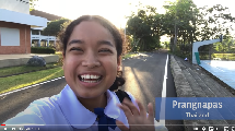 A girl smiles and waves into the frame.