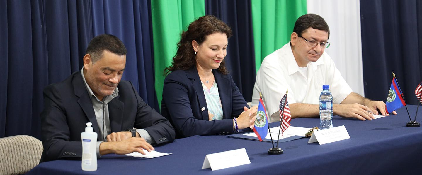 Two men and one woman sit at a table ready to sign documents.