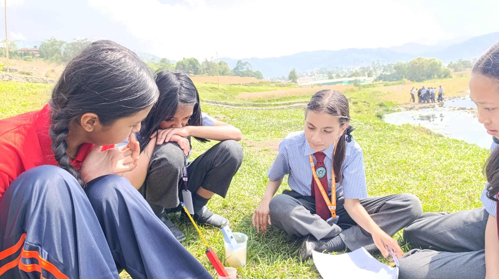 Student sitting on grass working with a cup of water and equipment.