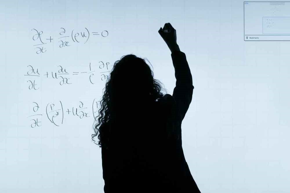 Photo of a woman working an equation on a board. Credit: QSIDE