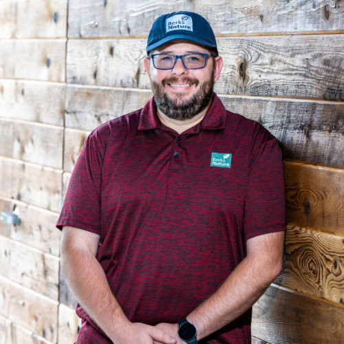 Michael Griffith stands in front of a wooden wall and smiles at the camera