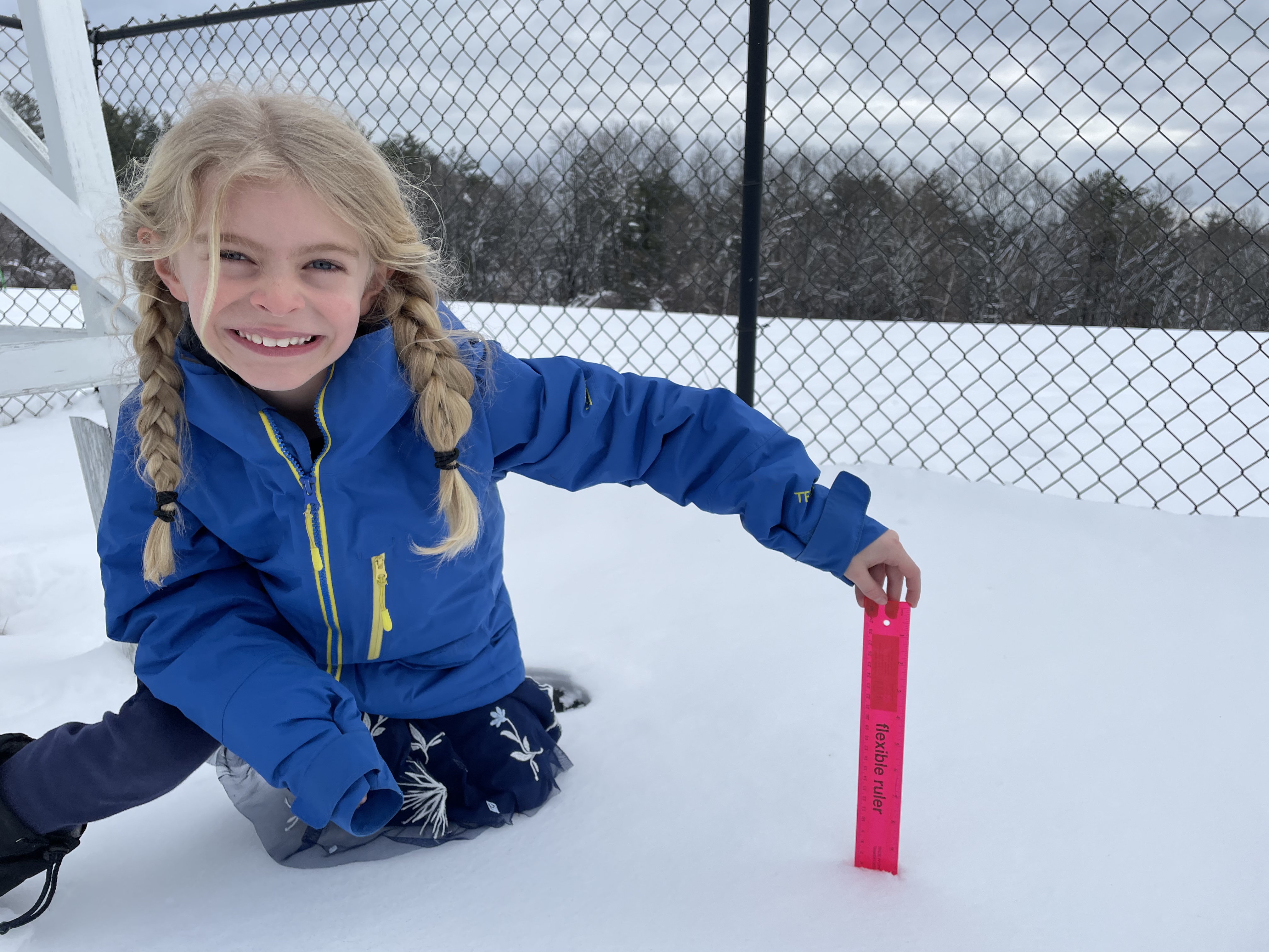 a young student holds a ruler in snow to measure snow depth