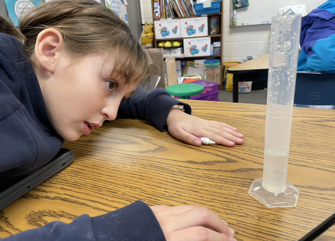 a student sitting a table with a graduated cylinder containing water to measure snowpack liquid equivalent
