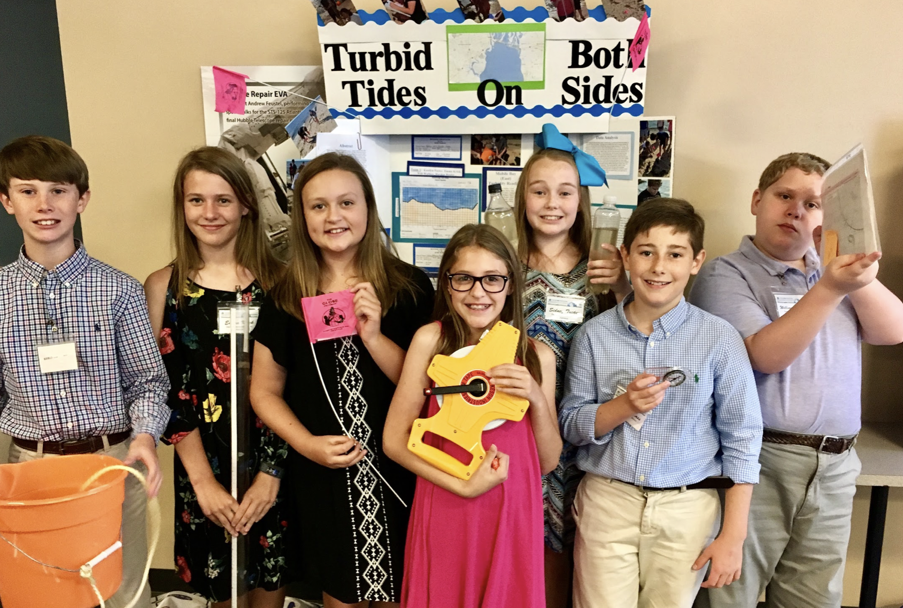 students hold up research equipment in front of their presentation poster