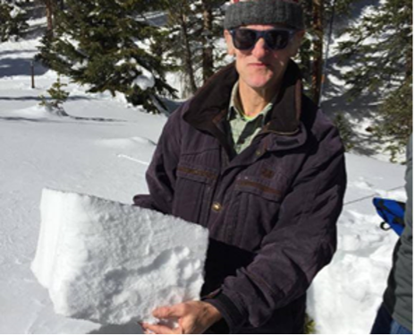Richard Wagner holds a block of snow while standing outdoors in a snowy setting