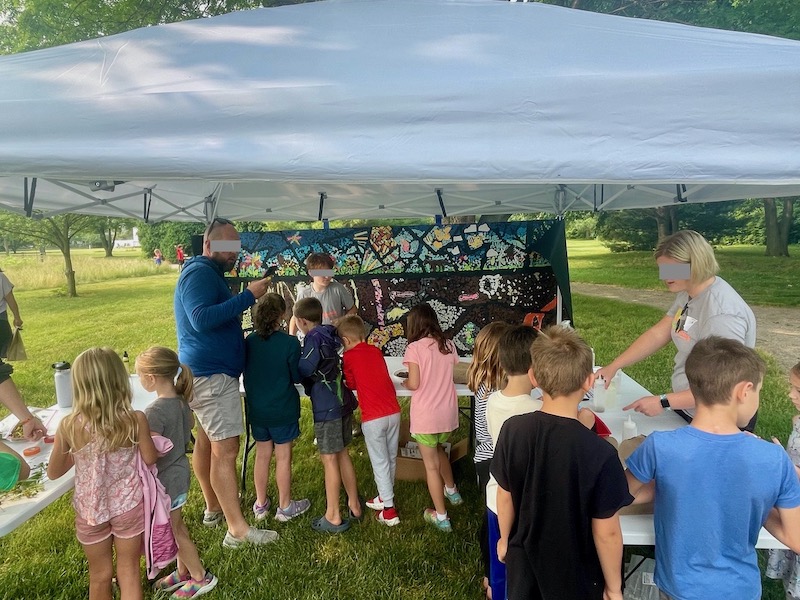 students and adults investigate soil at the Soil and Solar Festival with the soil mural hanging in the background