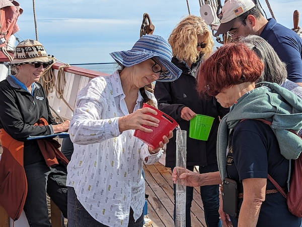 Nico Janik pours water from a bucket into a transparency tube as other attendees conduct other water measurements