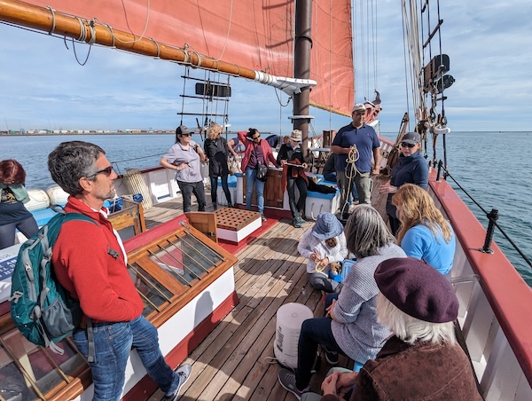 Pacific North American Regional Meeting attendees sit and stand on a tall ship while collecting water samples 
