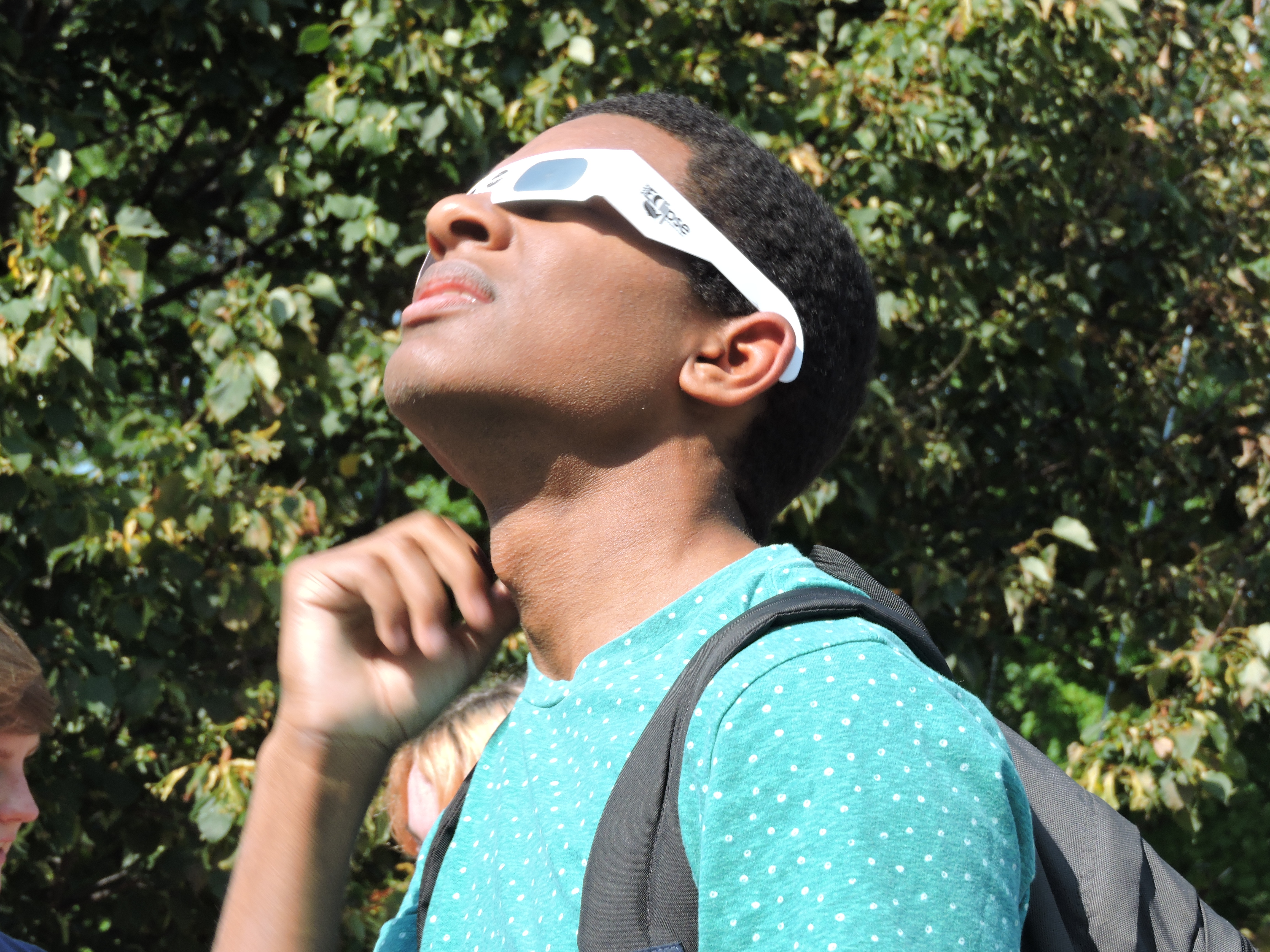 young male student looking up through eclipse glasses