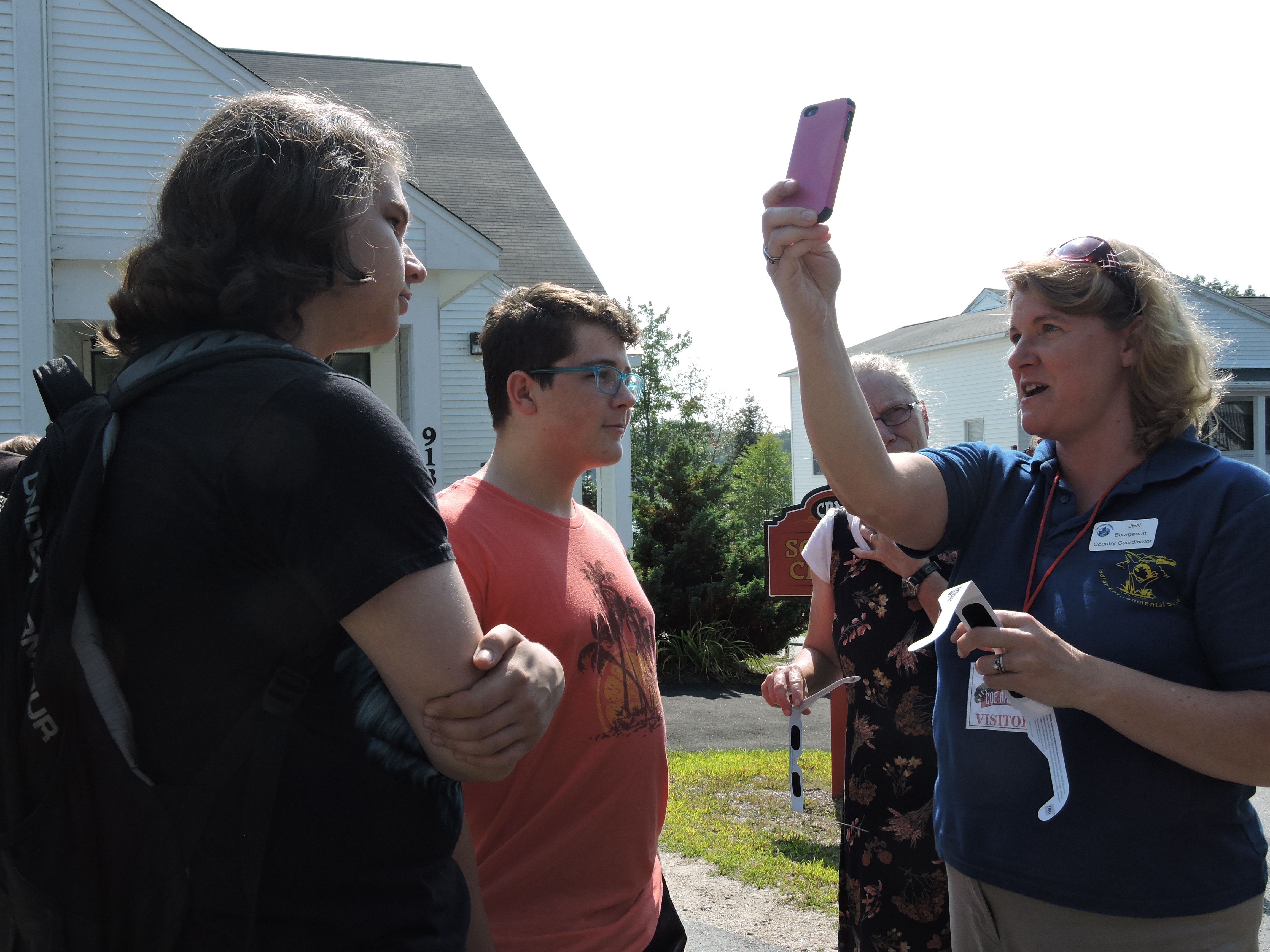 bourgeault with observer app and eclipse glasses in hand explaining to two young male students and one adult female how to take the pictures with the app
