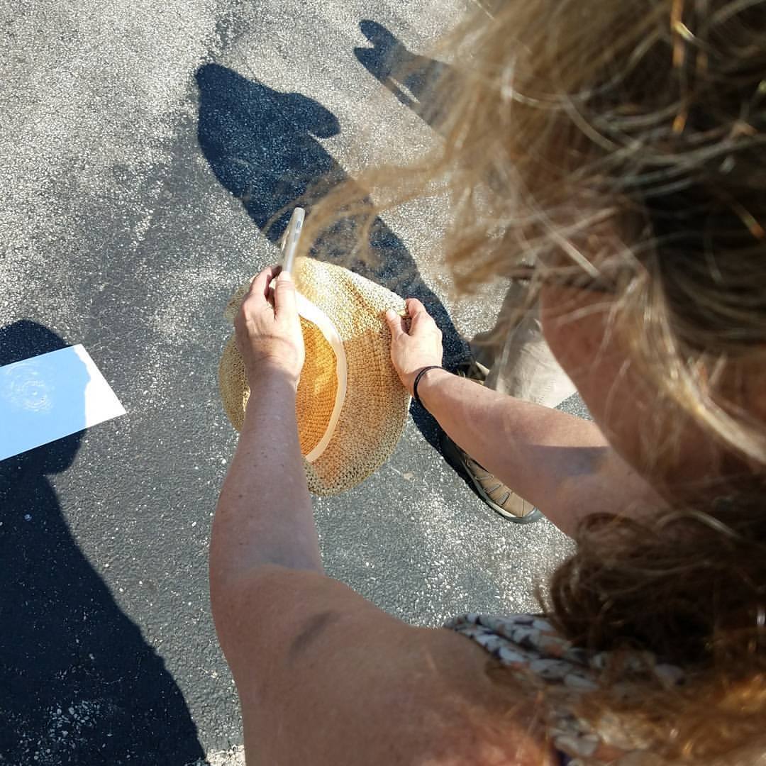 woman folding a straw hat making a basket shape toward the ground to stream sunlight through it. a white piece of paper is on the pavement