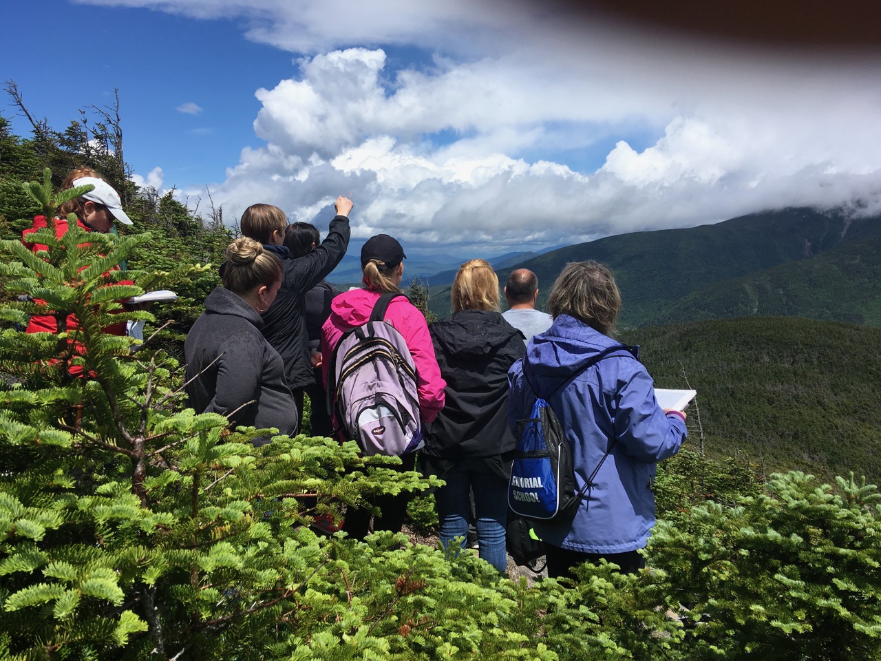 teachers on the mountain looking off into the distance qith blue skies and white fluffly clouds